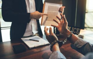 A person in handcuffs is speaking with a lawyer reviewing legal documents.