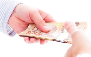 Close-up of hands exchanging Canadian $100 bills.