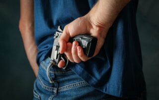 A man hiding a handgun behind their back.