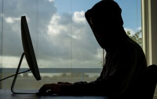 A person in a hoodie is using a computer in an online obscenity crime.