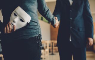 A person shaking hands while hiding a white mask behind their back.