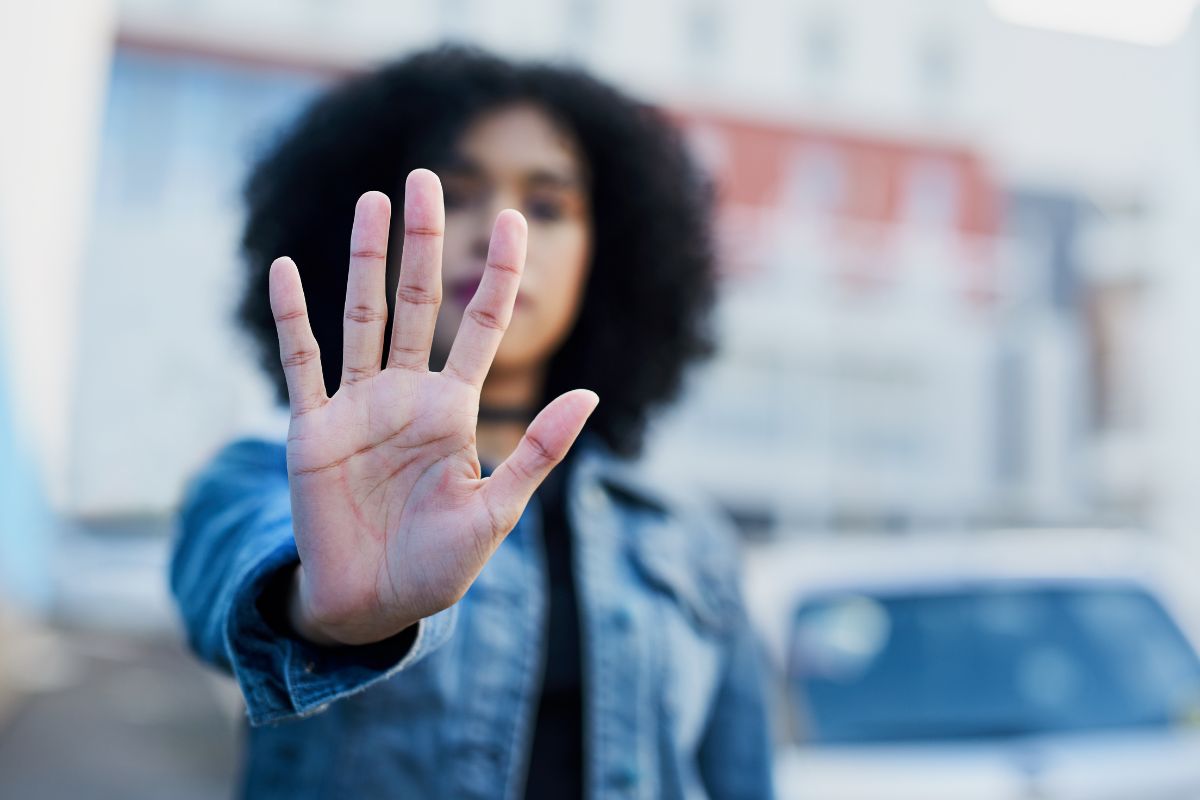 A woman standing outdoors with her hand raised. A woman standing outdoors with her hand raised.
