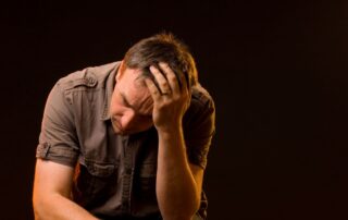 A distressed man sitting with his head in his hand.