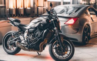 Black motorcycle and silver sports car parked.