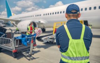 Airport ground crew checking luggage near an airplane.
