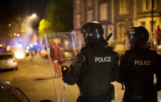 Police officers in full riot gear with shields raised.