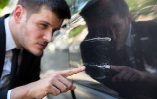 Man inspecting a scratch on a car door.