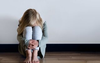 A scared young girl sitting on the floor.