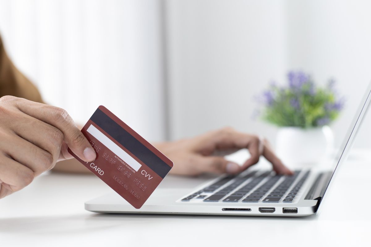 A person holding a credit card while using a laptop. A person holding a credit card while using a laptop.